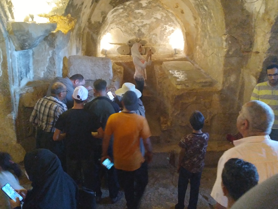 People can visit inside the cave. There are several large graves with their side facing the Qibla. The people on the left are looking into one of the graves through a glass window.